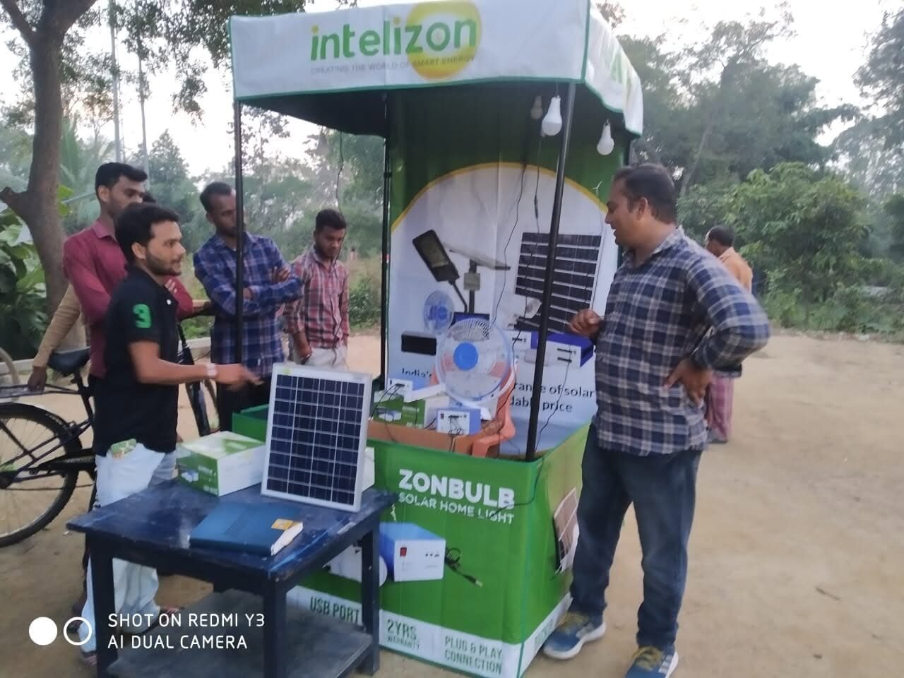 Intelizon branded solar product kiosk at a village camp with people checking solar panels and lights