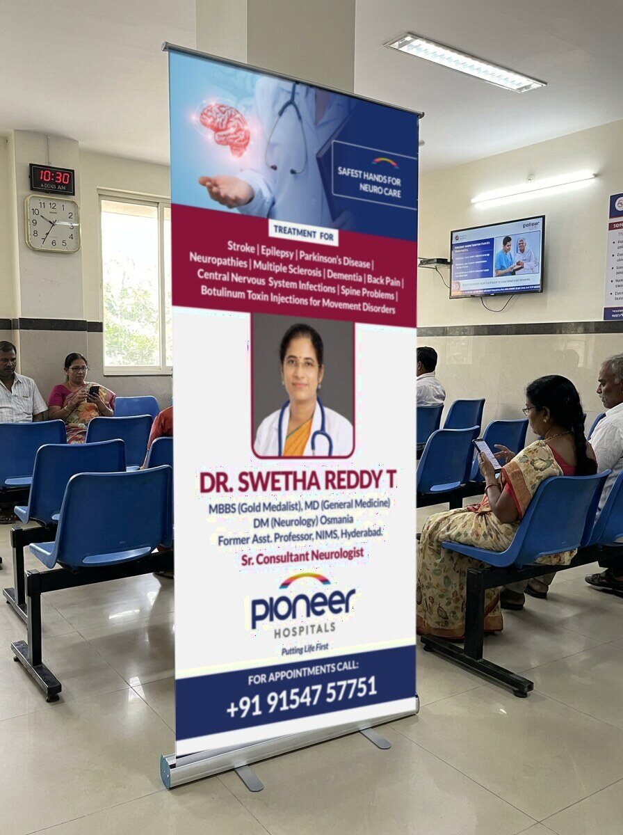 Pioneer Hospitals neurology standee for Dr. Swetha Reddy T in the OPD waiting area with patients on blue chairs, photo mockup